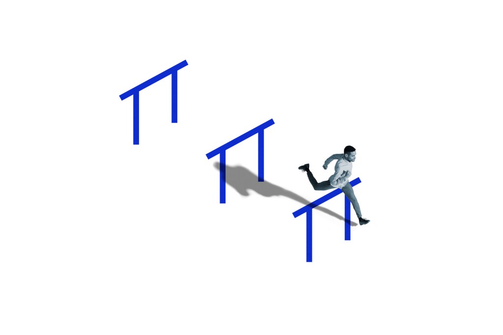 High angle side view of young man jumping over blue obstacle while running in hurdle race over white background.