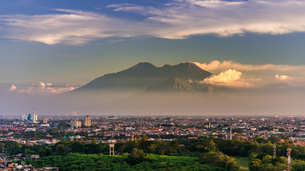 Skyline portrait of Surabaya in Indonesia, with mountains in the back and buildings in the front, used in a post about Komunal