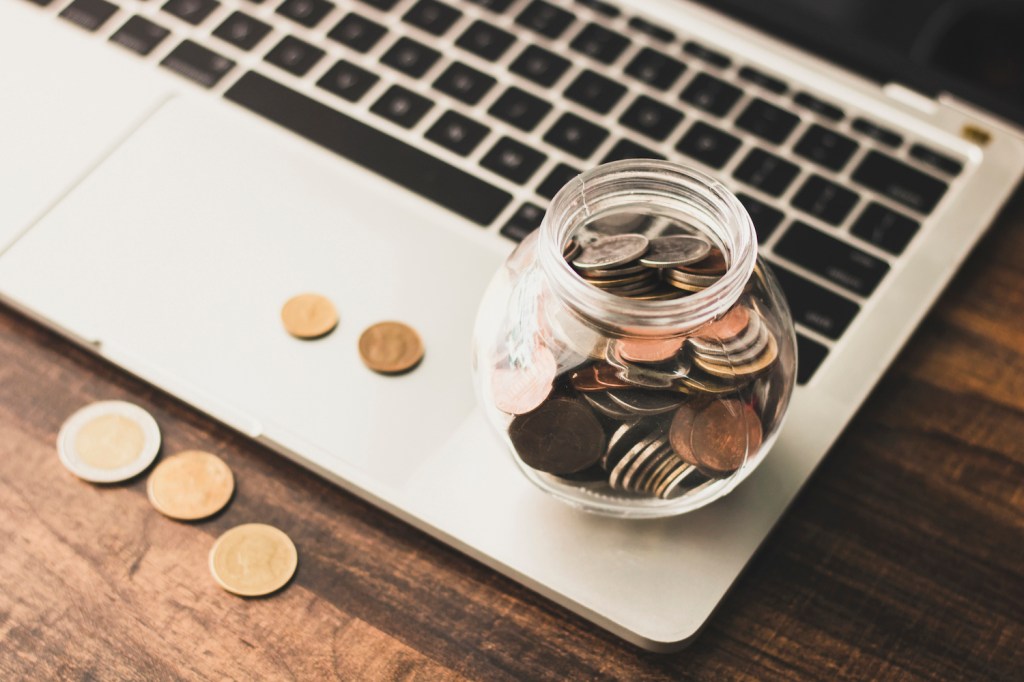 save and finance concept, money coins in jar with laptop on table