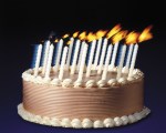 A frosted cake with candles that are being blown upon, as if someone just out of frame were making a wish.