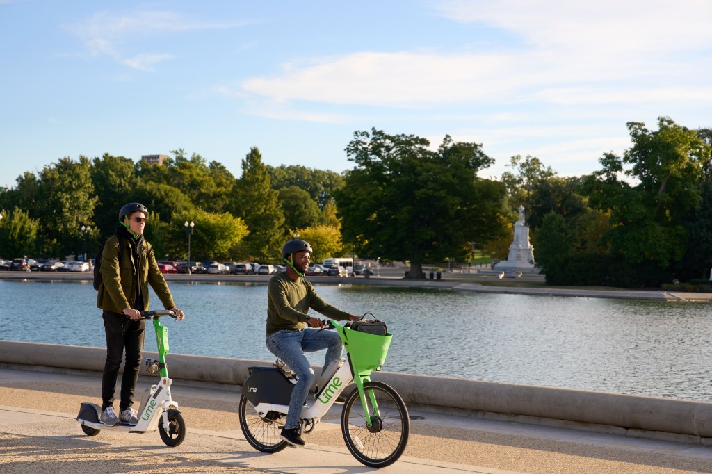 two men, one on lime e-scooter and one on lime e-bike, riding in front of a pond