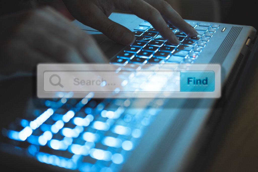 Concept de recherche montrant une zone de recherche superposant les mains d’une femme sur un clavier entrant une requête de recherche.