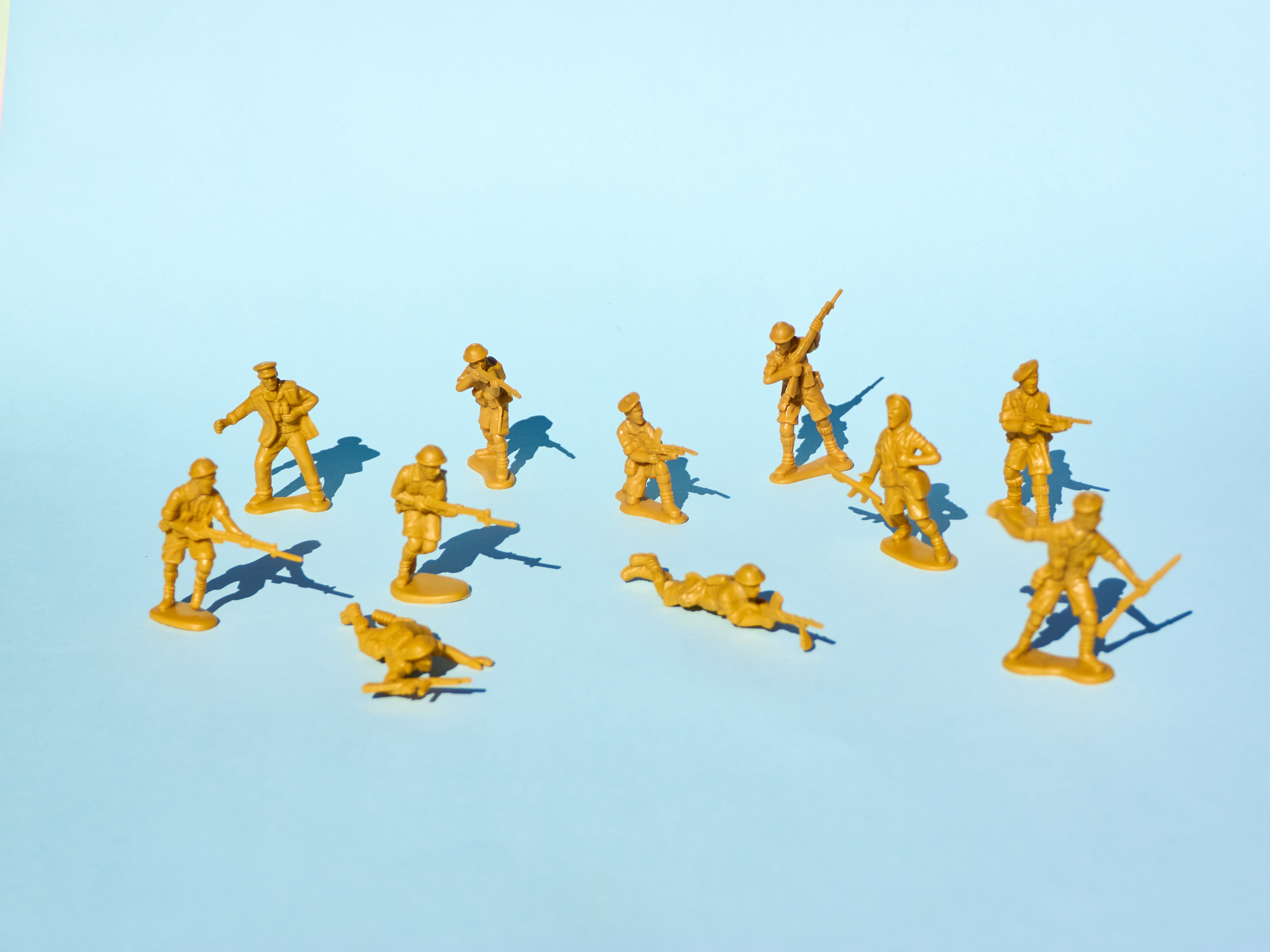 青色の背景に、互いに銃を向けている黄色のプラスチック製のおもちゃの兵隊のグループの画像。