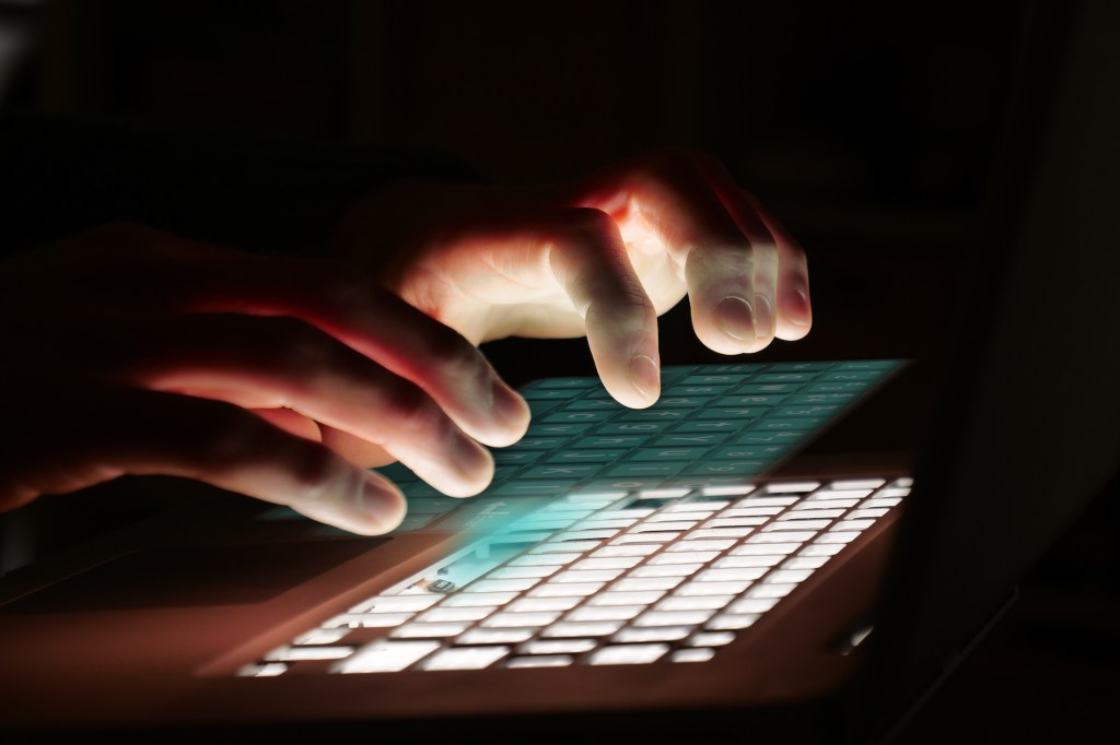 fingers typing on a hologram of a keyboard over a backlit keyboard in the dark