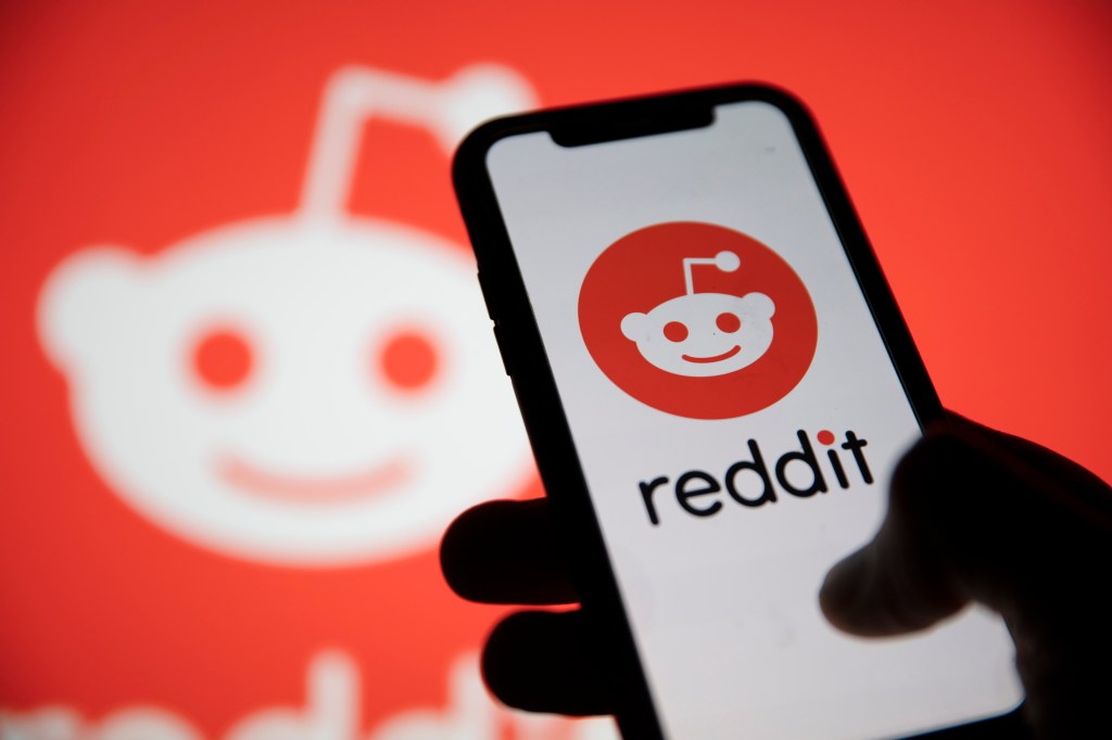 El logotipo de Reddit se muestra en el teléfono inteligente con el logotipo de Reddit de fondo.