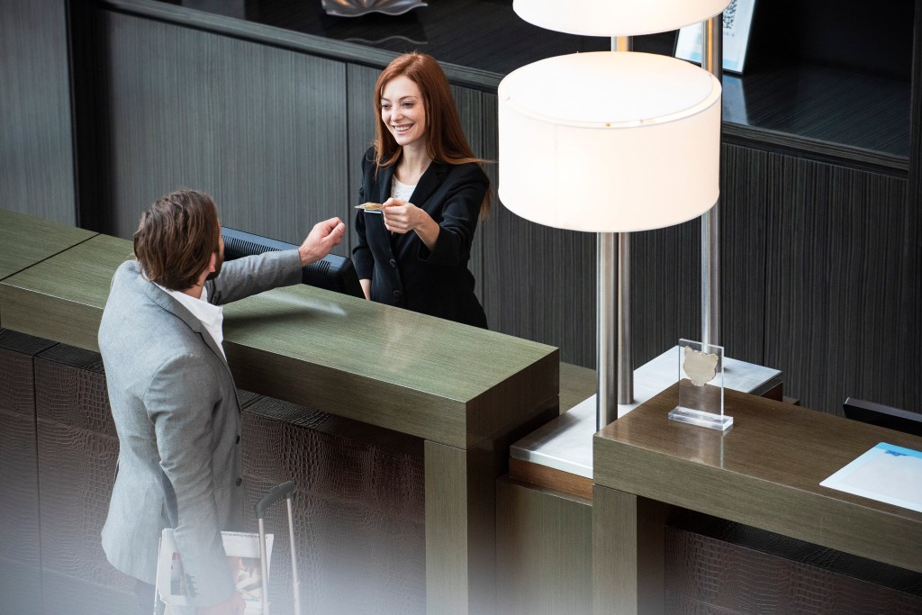 Smiling female receptionist giving credit card to businessman while standing at hotel reception