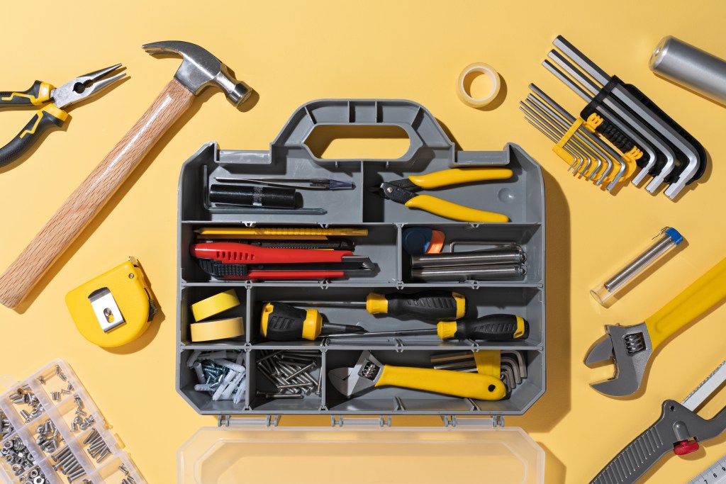 Opened DIY Toolbox With a Collection of Tools on Yellow Colored Background Directly Above View.