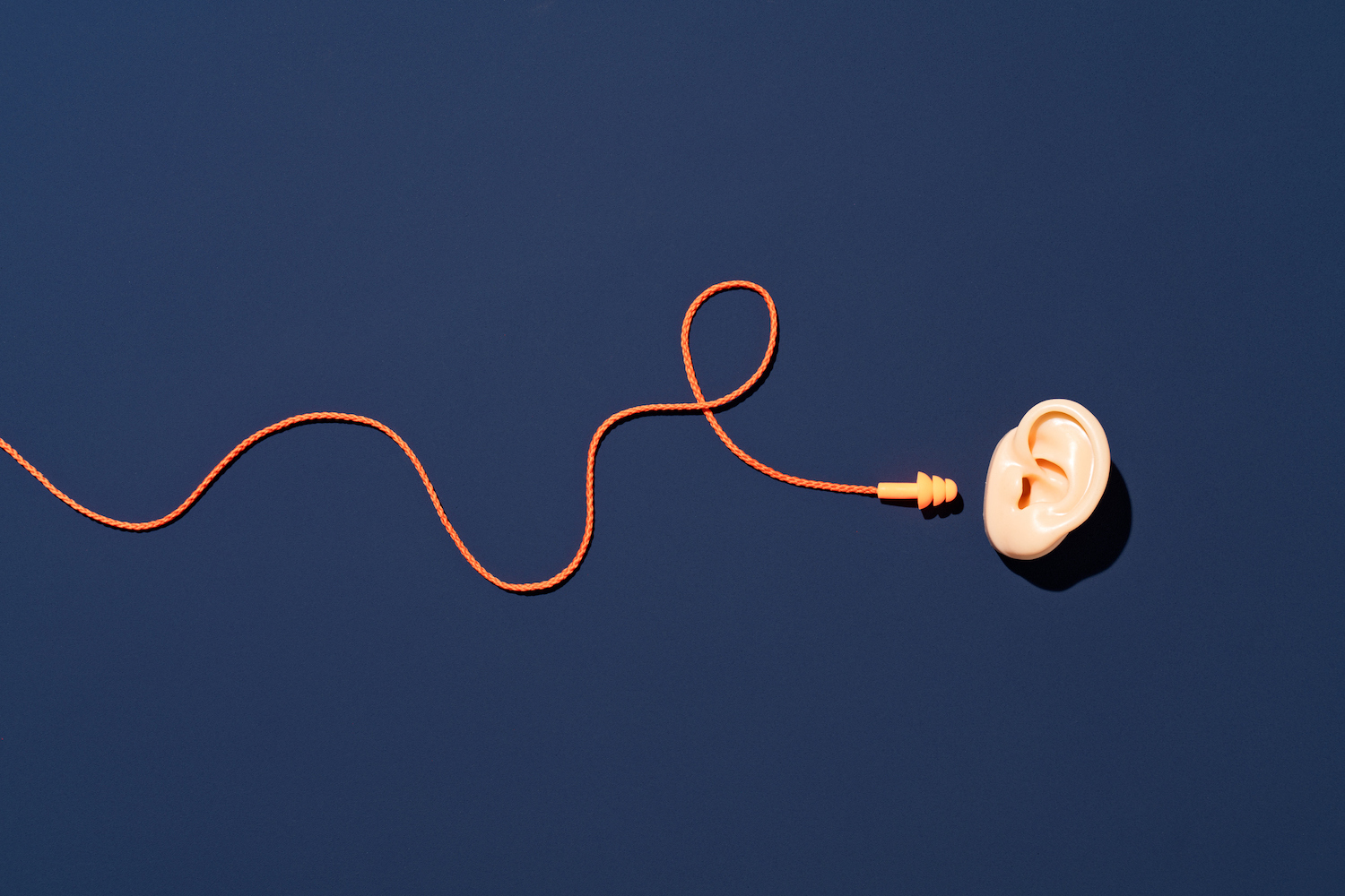 Tampões de ouvido laranja com corda curva alcance a orelha no fundo azul diretamente acima da vista.  4 dicas para as equipes de RevOps filtrarem o ruído e focarem no quadro geral