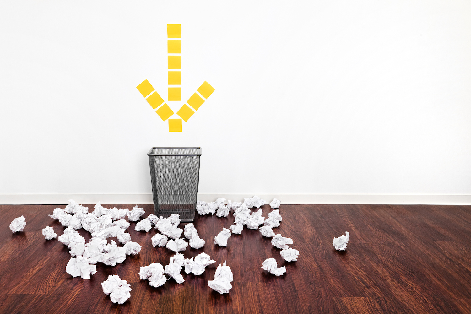 "Failure" Office Metaphor a wastebasket with an yellow arrow pointing to it that is surrounded by crumpled paper balls.
