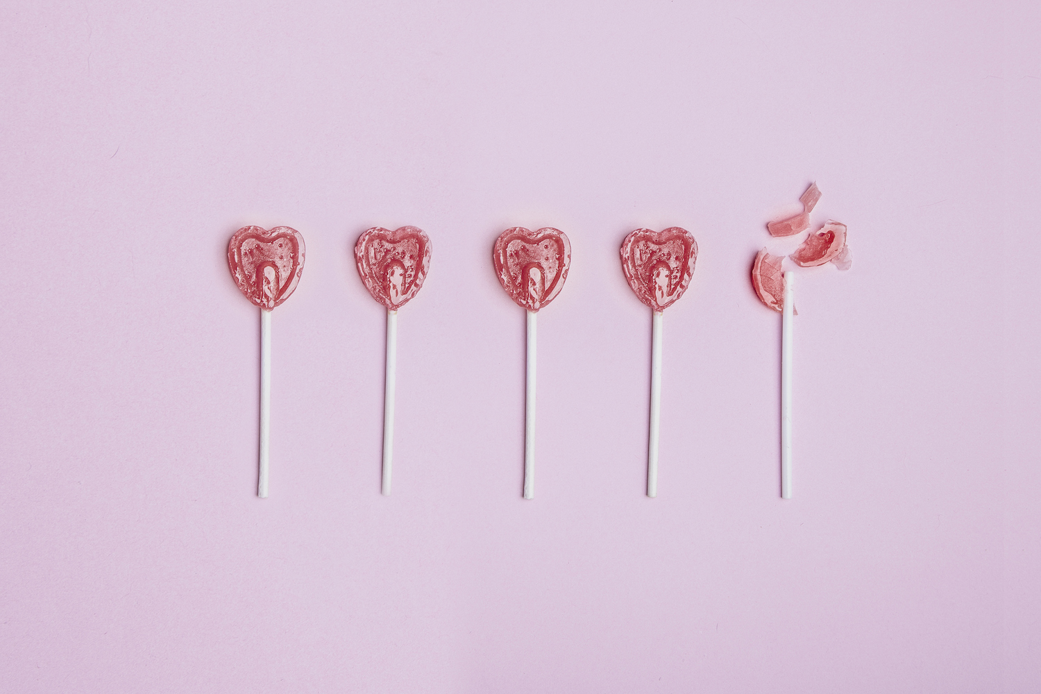 Five lollipop hearts on a pink floor but the last one is torn to pieces.