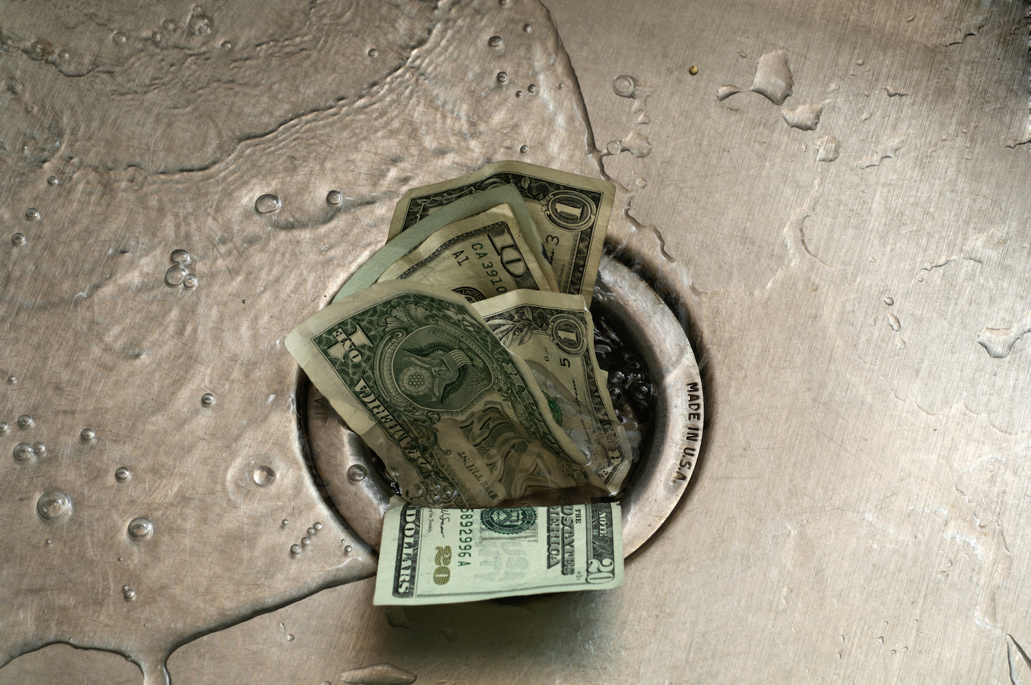 El papel moneda estadounidense es empujado por el desagüe de un fregadero húmedo