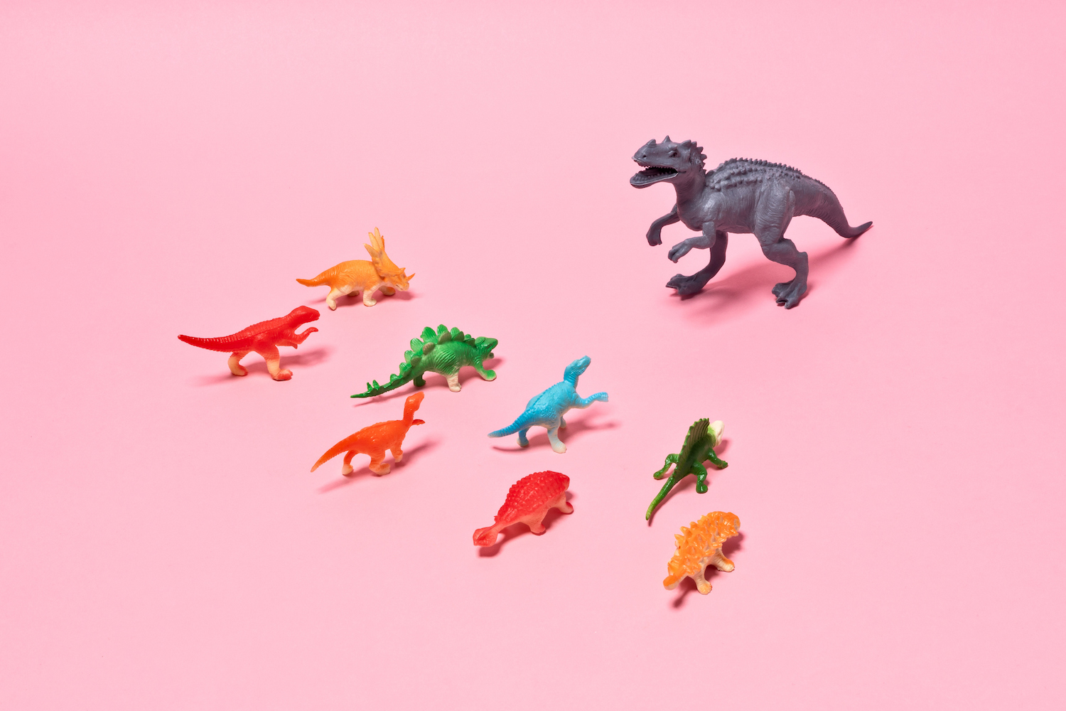 Toy Dinosaurs Confliction, Rex Dinosaur Standing Out From the Crowd on Pink Background.