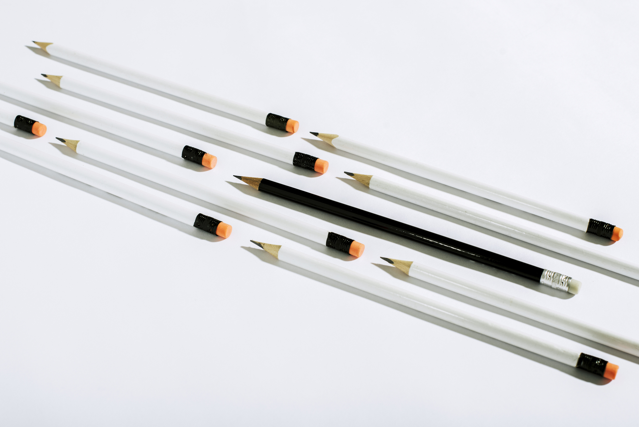 Row of white pencils and one black pencil, lying on a white background
