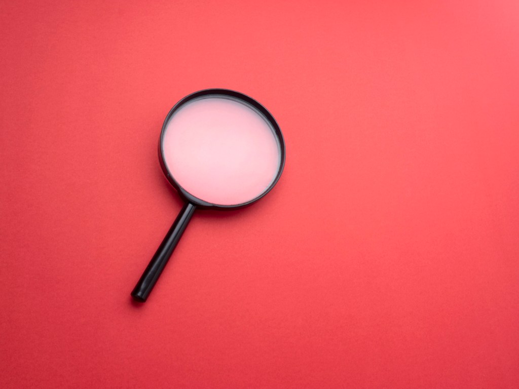 Magnifying glass on red colored background.