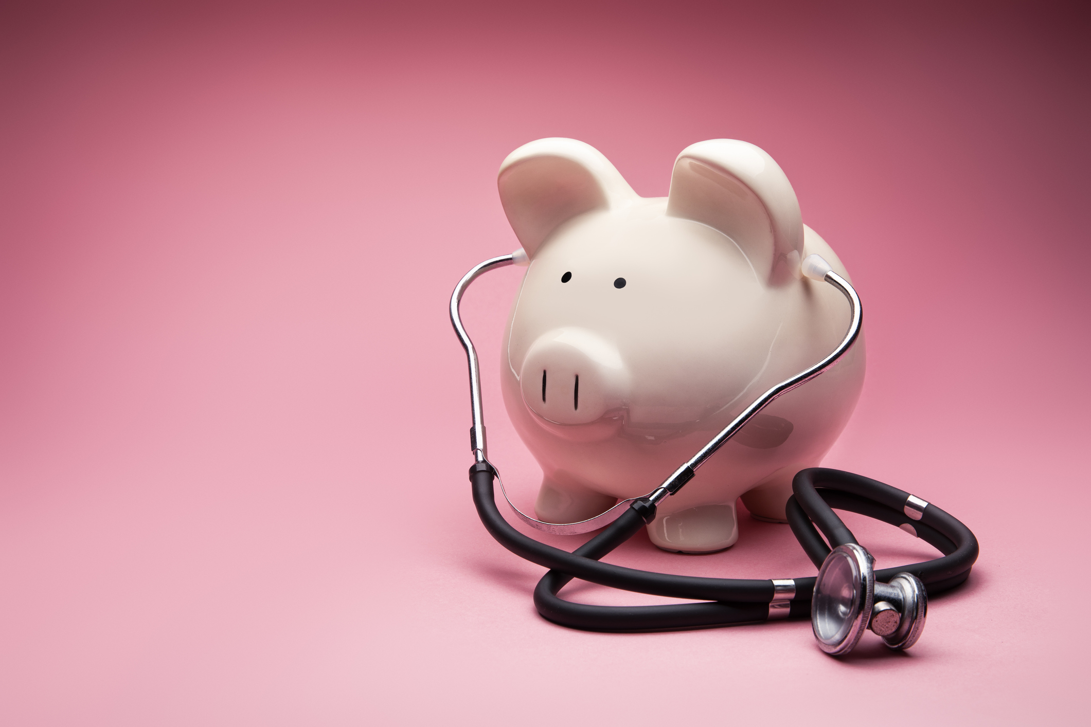 image of a piggy bank with a stethoscope on amid a pink background.