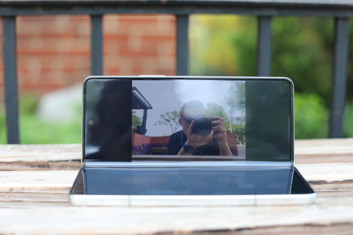 Samsung galaxy z fold 5 روی یک نیمکت بیرونی که صفحه دوربین را منعکس می کند