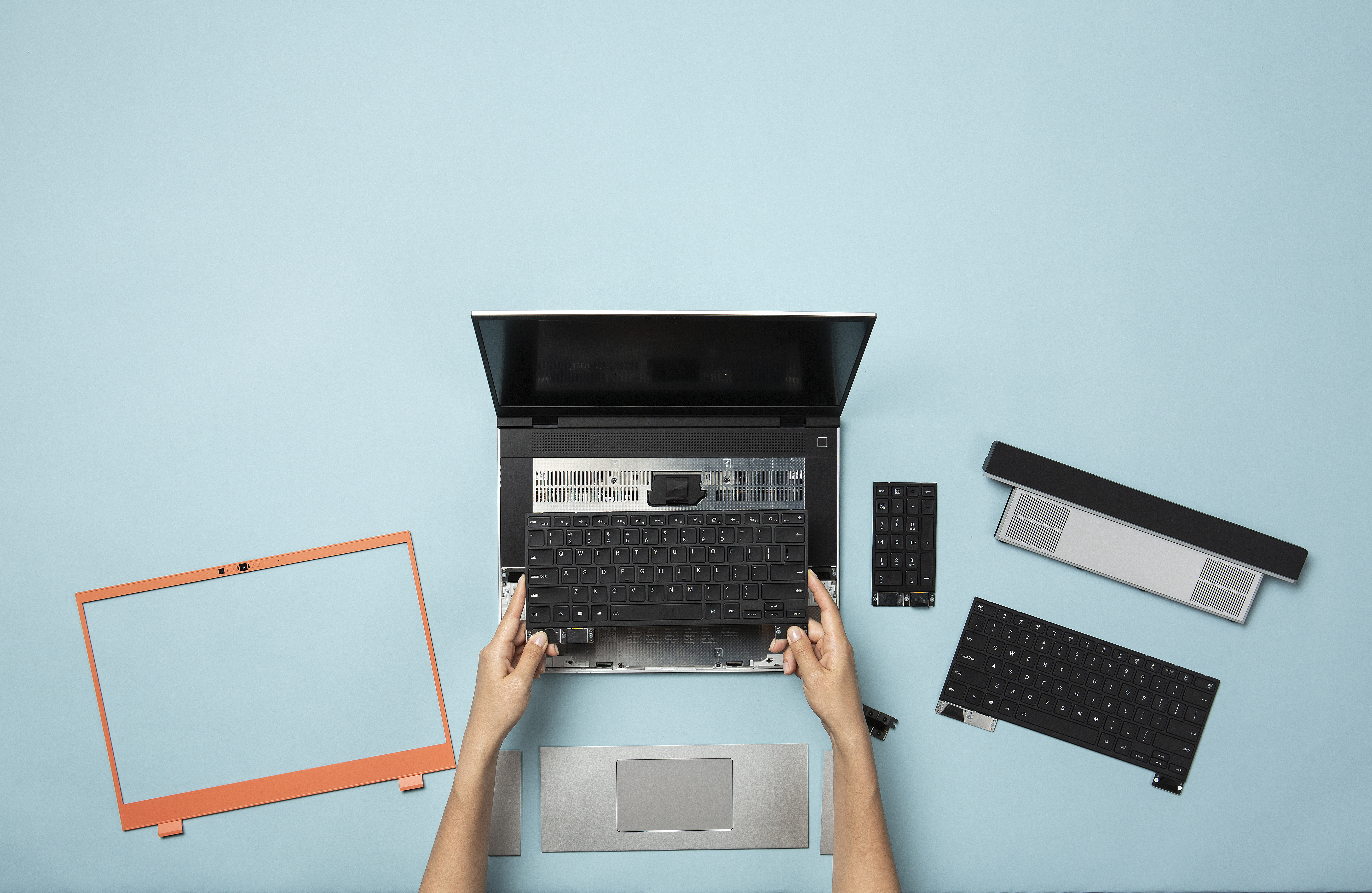 An image depicting two hands touching Framework's new Laptop 16 with laptop components surrounding the device