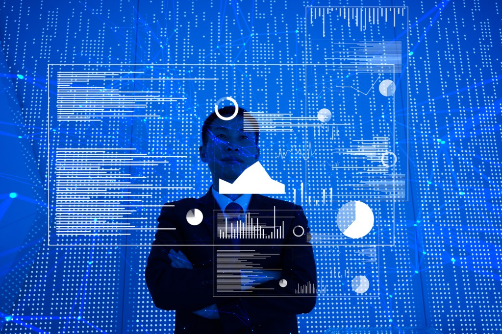 Man standing in front of a large blue screen with graphs and data spread out in front of him.