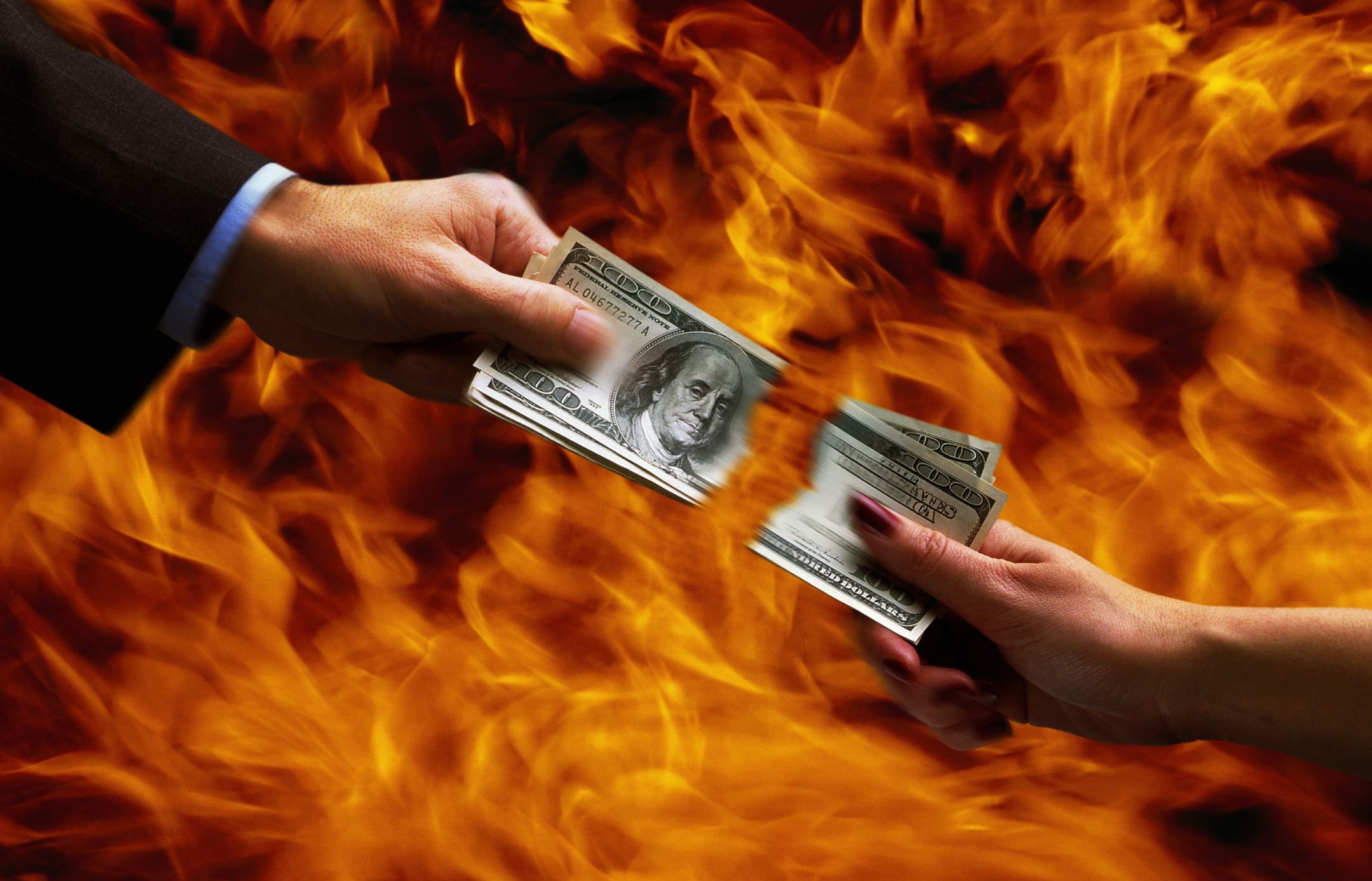 Hände von zwei Menschen, die Geld zerreißen, mit Flammen im Hintergrund