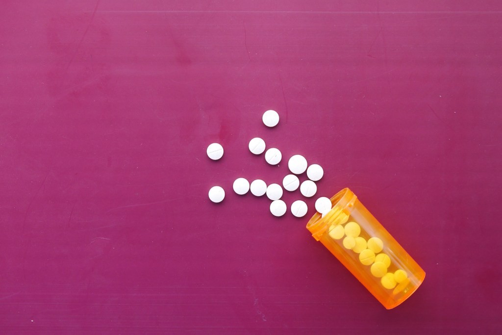 white medical pills scattered on pink