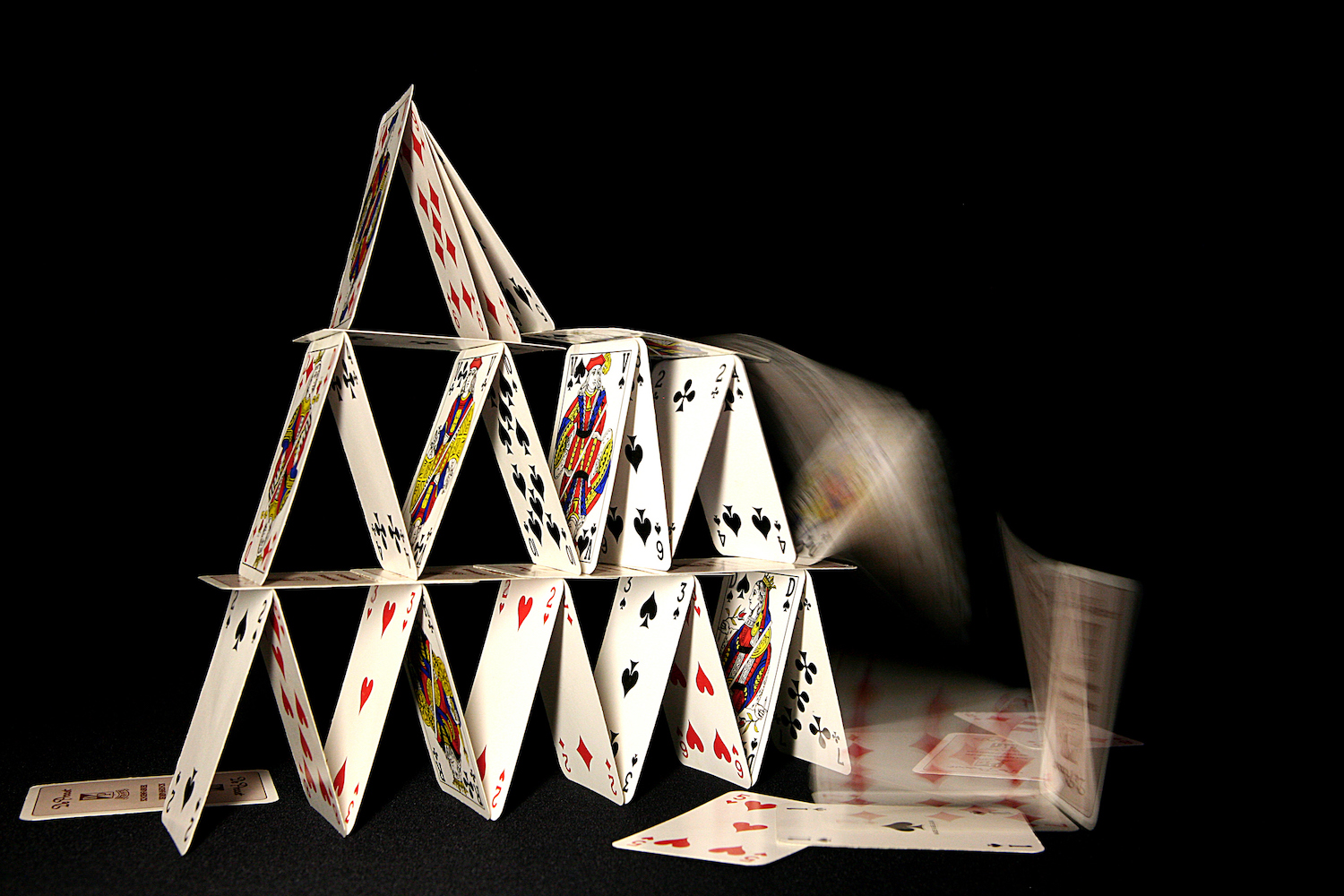 A house of cards collapsing on dark background