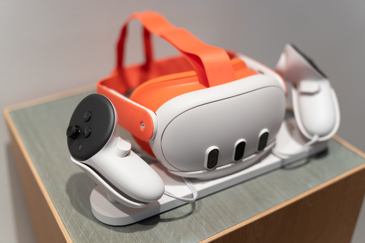 The Meta Quest 3 mixed reality headset, sitting on a first-party charger with an orange headstrap