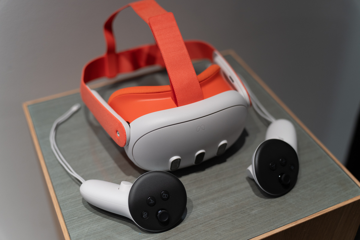 The Meta Quest 3 mixed reality headset, sitting on surface with an orange head strap and face pad