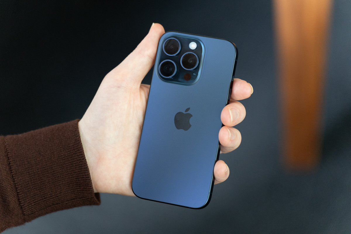iPhone 15 Pro in blue titanium held in a hand, showing the back of the phone