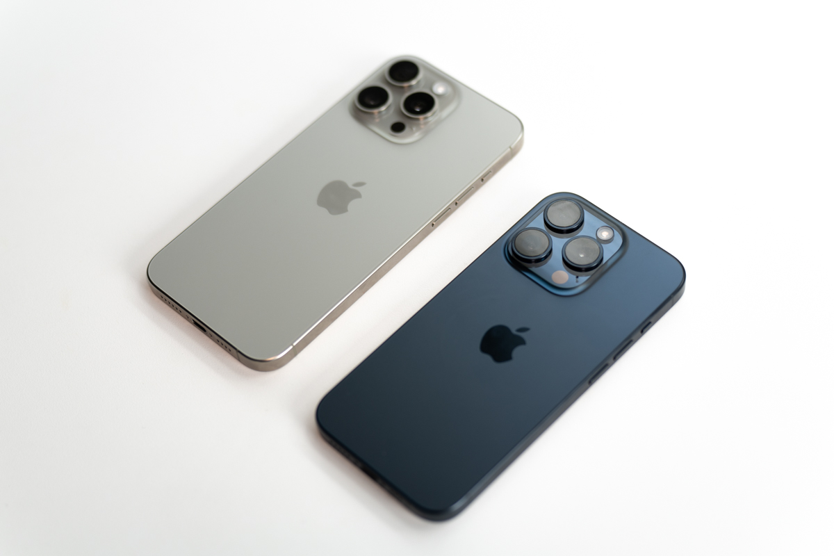 The natural titanium iPhone 15 Pro Max, and the blue titanium iPhone 15 Pro side-by-side, face down on a table