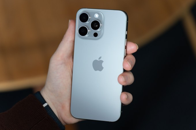 iPhone 15 Pro Max hecho de titanio natural, sostenido, mostrando la parte posterior del teléfono