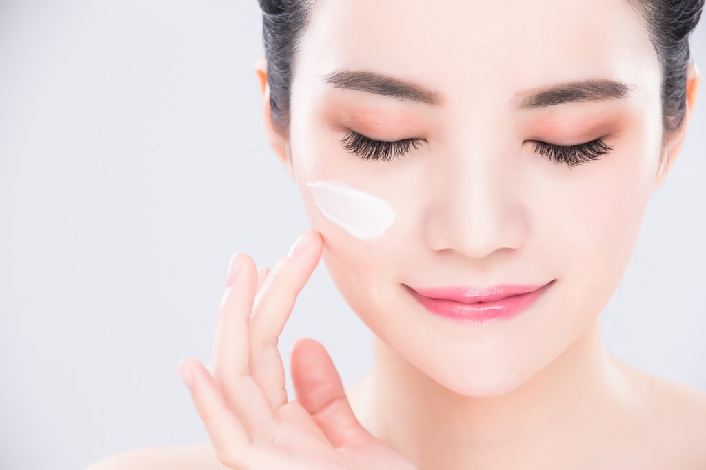 East Asian woman closes eyes while applying skin cream