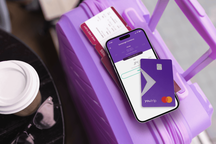 A smartphone on a purple suitcase displaying YouTrip's FX exchange app. On top of the smartphone is one of its cards.