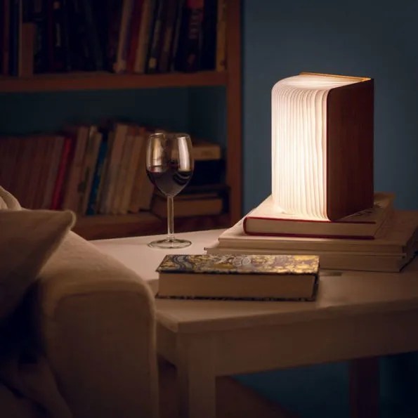 A wooden booklight sat open on a desk next to a book and wine glass