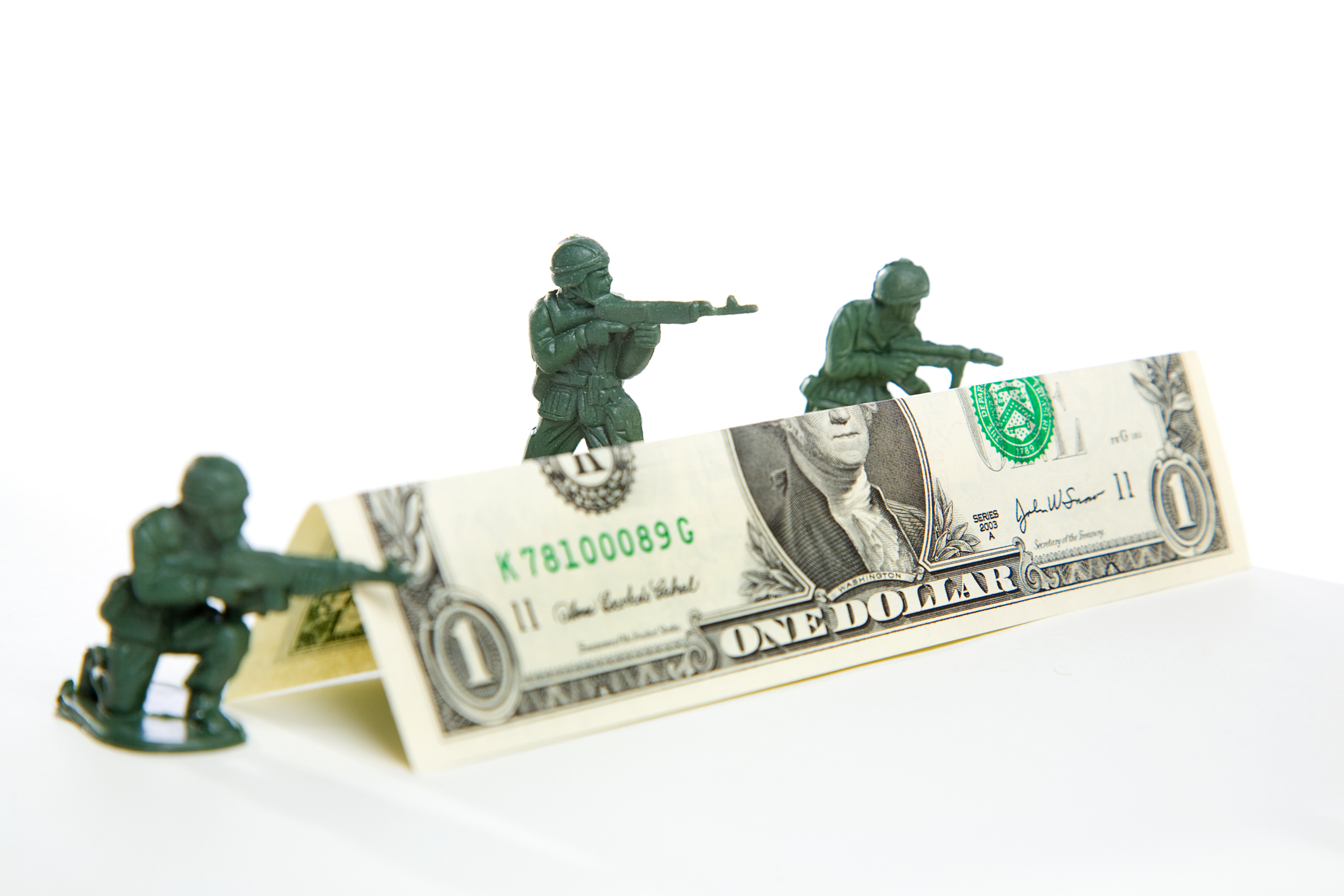 Three plastic toy soldiers shooting over a barricade made of a folded dollar bill