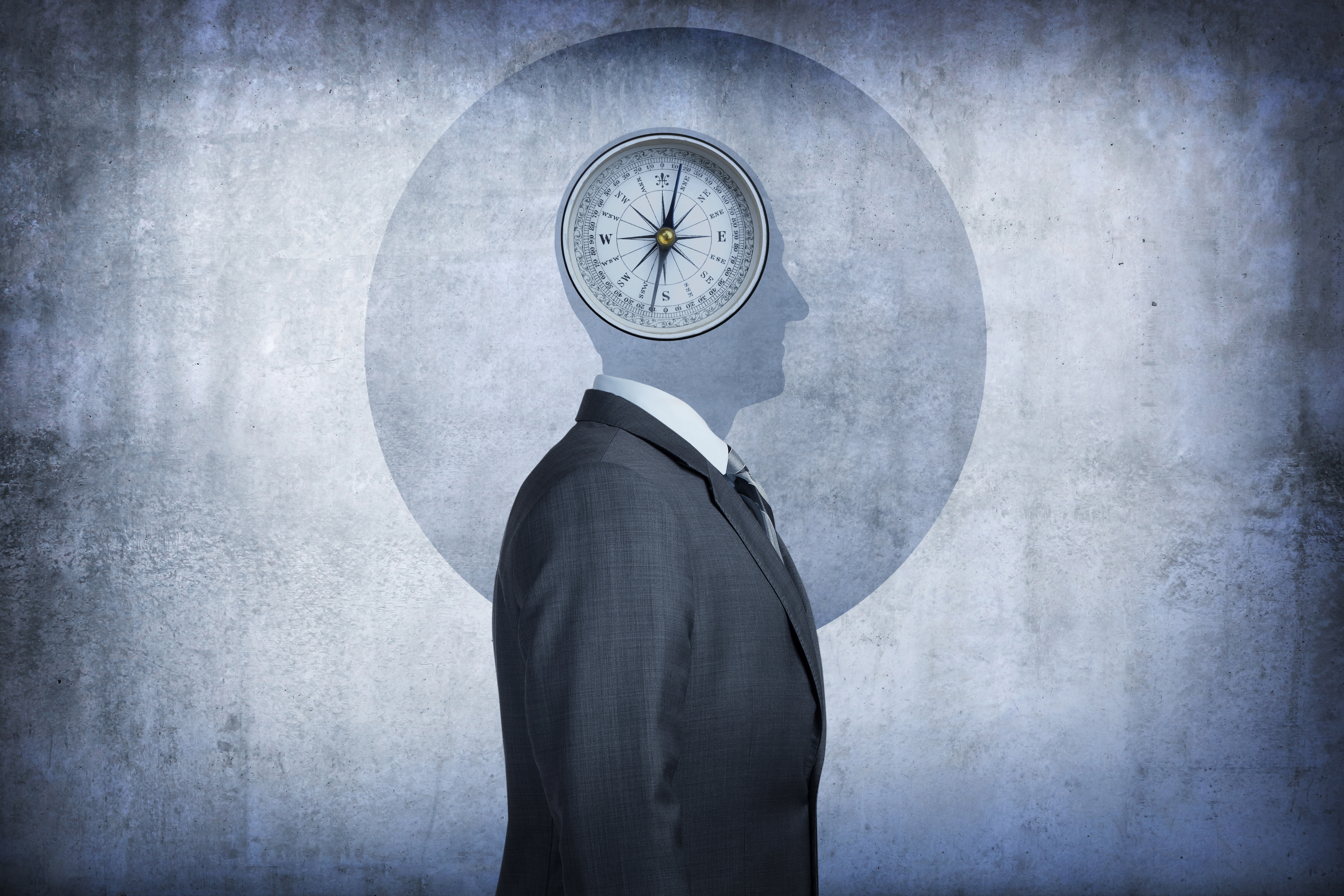 A compass occupies the space over the man's head conveying the concept of morality and the choices we make. The man's head is reduced to its simple shape, devoid of any detail, and is silhouetted against the background. The man, dressed in a suit, stands at a profile to the camera.