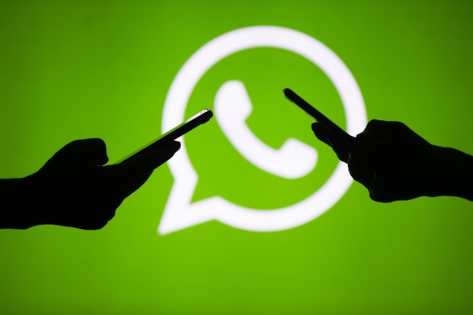 People hold mobile phones in front of the logo of WhatsApp application.