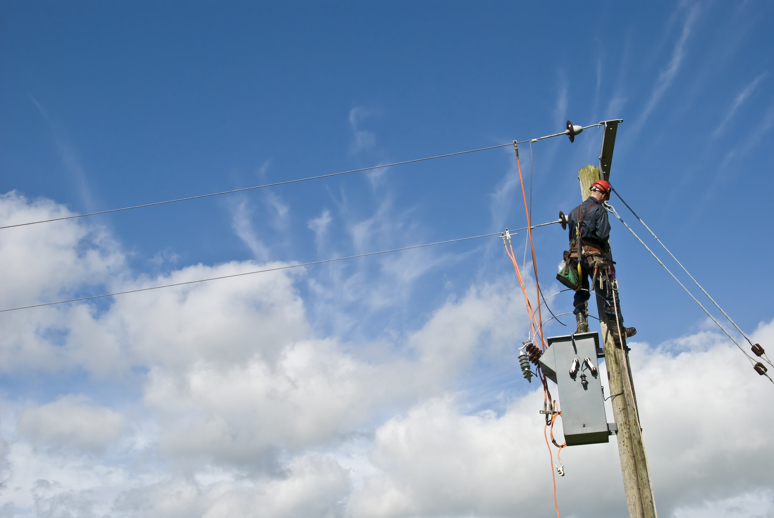 Utility worker repairing power lines under a blue sky