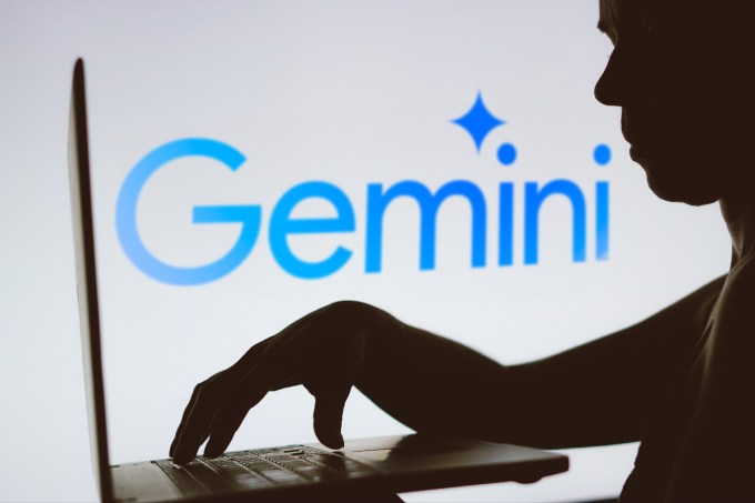 Logotipo de Google Gemini detrás de una persona que trabaja en una computadora portátil